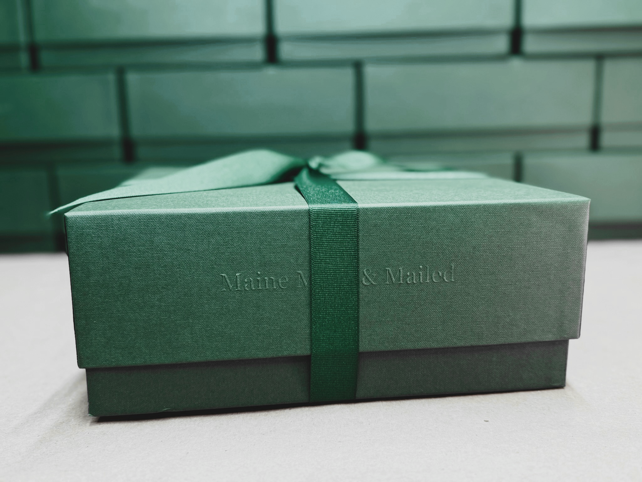Green gift box with a ribbon and 'Manned & Mailed' branding on a light gray surface.