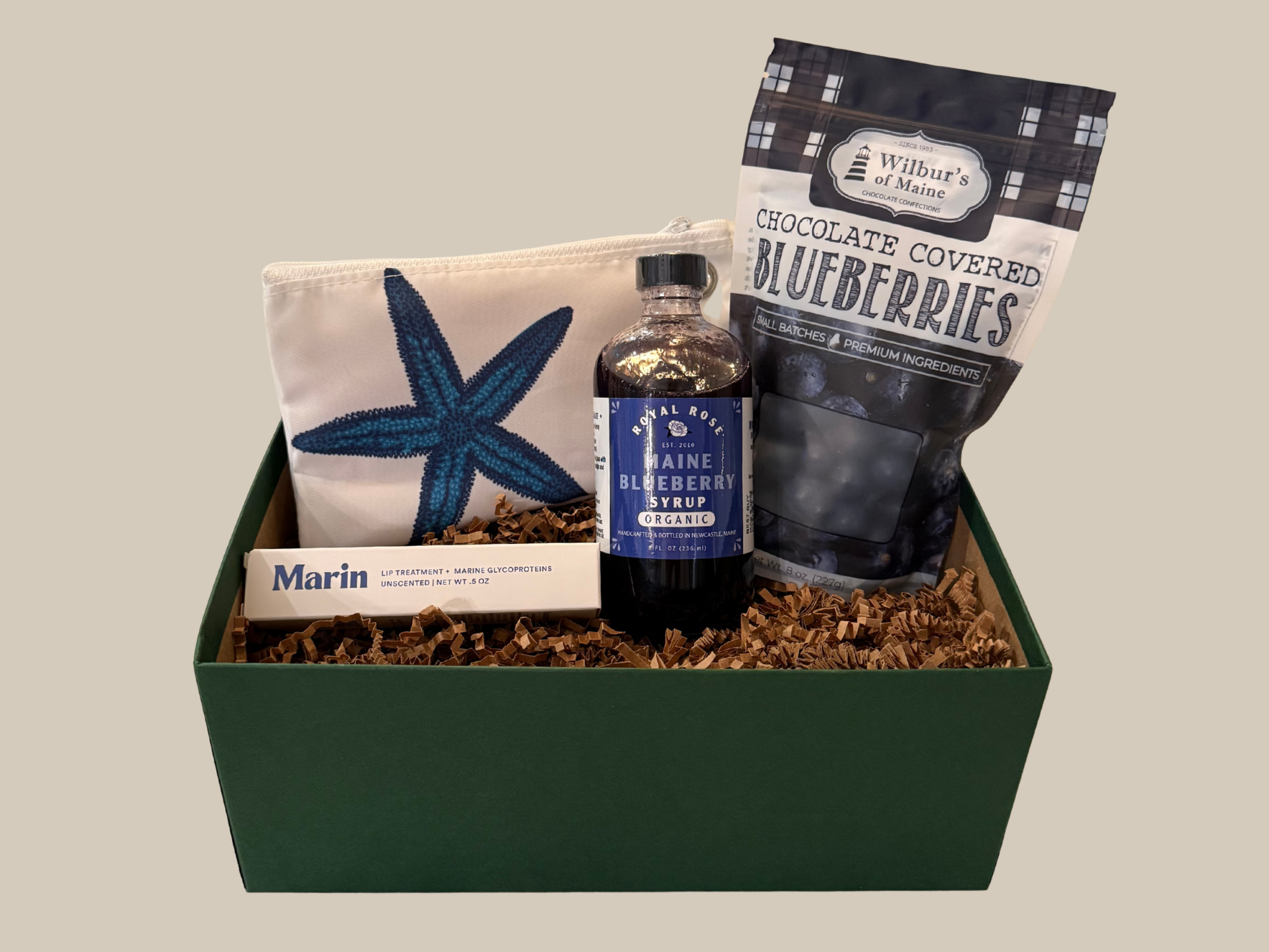 Gift box with a bottle of blueberry syrup and a bag of chocolate-covered blueberries on a beige background.