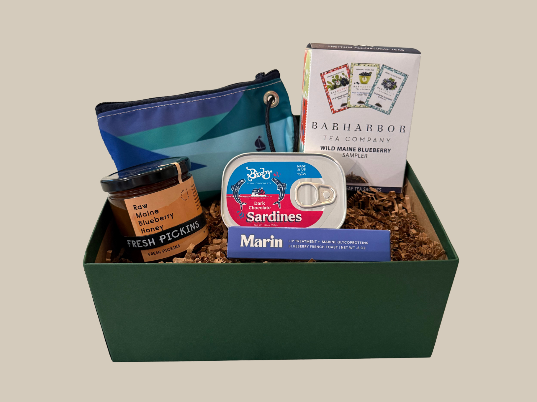 Gift basket with various items including a can of sardines, honey, and a pouch on a beige background.