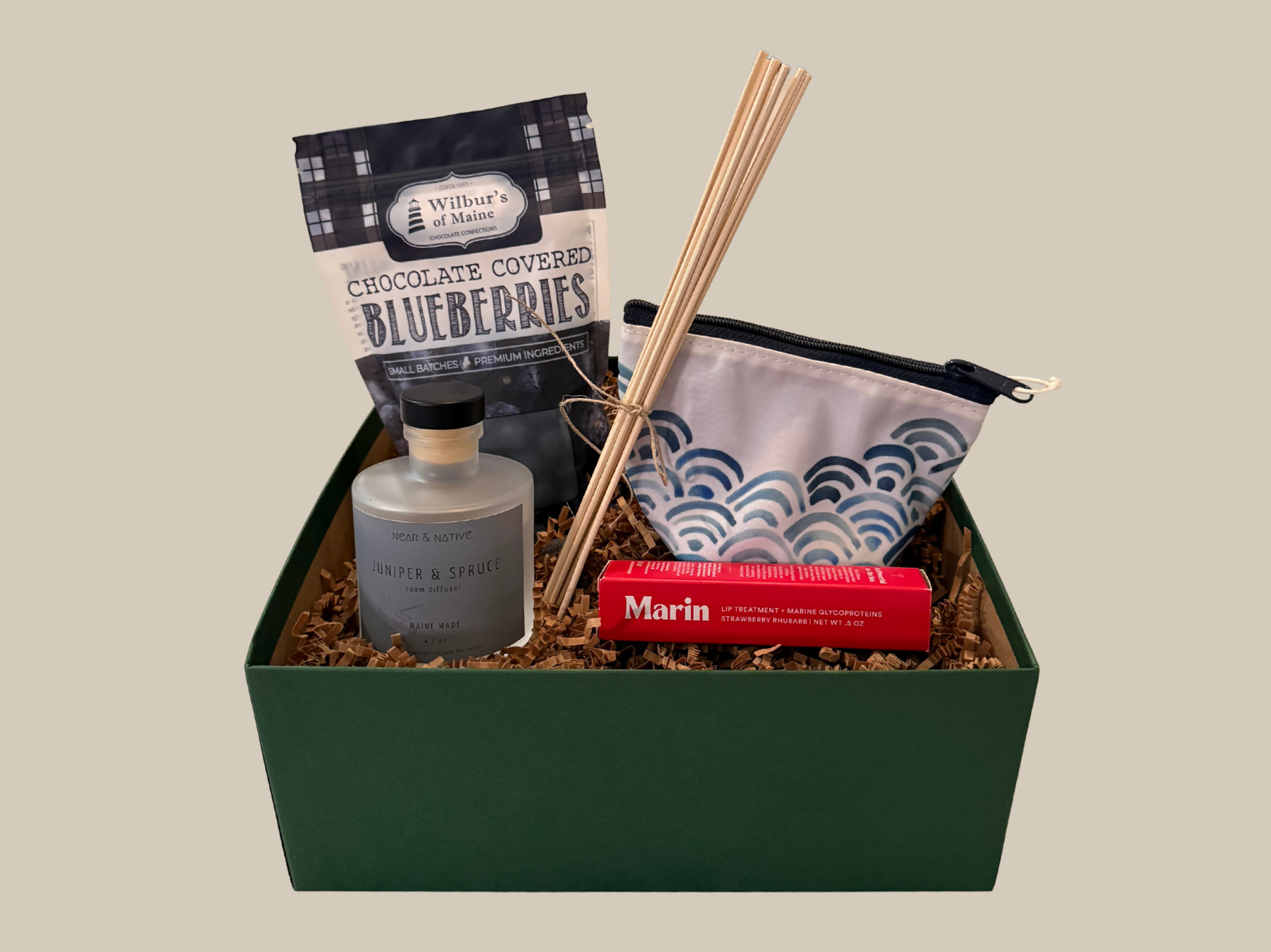 Gift box with a bottle, snacks, and a pouch on a beige background